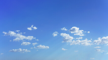 Wall Mural - fluffy white clouds down to horizon with blue sk and faint sunbeams.