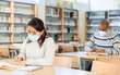© JackF - Young adult woman in protective face mask working with books, finding information at library