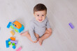 © Tina kids photo - baby in a gray bodysuit is playing with a multi-colored constructor sitting on the floor. top view