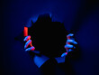 © golubovy - Breakthrough background. Night mystery. Red blue neon light female hands tearing paper ripped wall isolated on dark black round frame empty space.