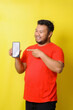 © Gatot - Attractive asian fat man in red tshirt is pointing finger to blank screen smartphone isolated on yellow background