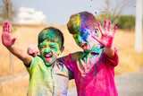 cheerful two Indian kids shouting by looking at camera after playing holi - concept of holi festival fun, siblings, and bonding.