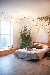 Wall Mural - Cozy bedroom area at luxury studio apartment with a free layout in a loft style with big panoramic window and green plant.