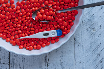 An electronic thermometer with a temperature mark of 39.7 in a large plate of red tablets with a tablespoon. The concept of dealing with high temperature