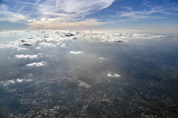  Aerial view from airplane window at high altitude of distant city covered with layer of thin misty smog and distant clouds