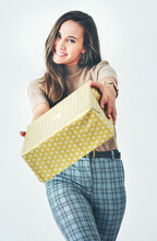 Heres A Gift From Me To You. Portrait Of An Attractive Young Woman Holding A Wrapped Present Against A Grey Background.