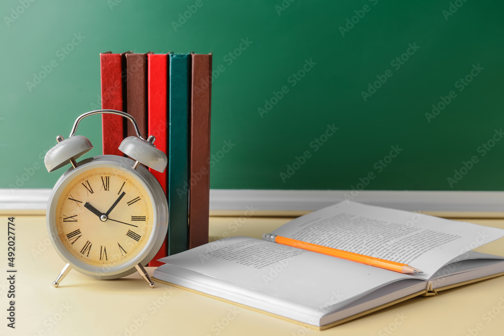 Books, alarm clock and pencil on table in classroom