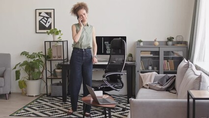 Full length slowmo of female software developer talking on smartphone with colleague while working with program coding on pc computer at home office