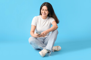 Poster - Beautiful young Asian woman with mobile phone on blue background