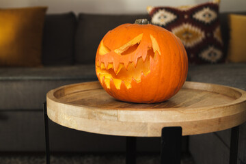 Carved Halloween pumpkin, jack lantern (Jack-o'-lantern). Spooky laughing, scary head on a small table in a home living room, with a couch in the background.