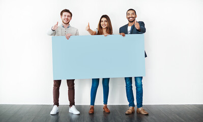 Poster - Go for it. Studio shot of a group of young people holding a blank placard and showing thumbs up against a white background.