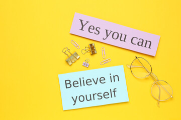 Wall Mural - Notes with motivational quotes, glasses and office stationery on yellow background, flat lay