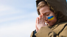 Ukrainian Boy Closed Her Eyes And Praying To Stop The War In Ukraine. Hands Folded In Prayer Concept For Faith, Spirituality And Religion. War Of Russia Against Ukraine. Stop War