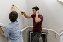 Father And Son Using Tape Measure, Measuring Wall Above Stairs