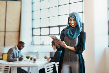 Canvas Print - She keeps track of the work progress in the company. Portrait of a confident young businesswoman browsing on a digital tablet while standing in the office at work.