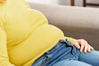 A close up of a woman with obesity that is caused by unhealthy food. Woman with hand on stomach to represent indigestion sitting on a couch