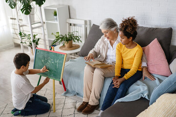 Wall Mural - Happy grandmother, nanny helping to mixed race grandchildren with study. Homeschooling concept