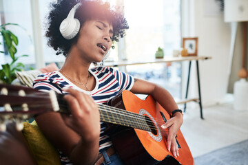 Poster - Music is a natural soother. Shot of a woman wearing headphones while playing the guitar at home.