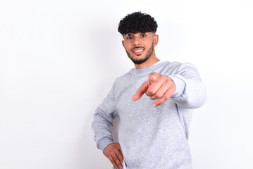 young arab man with curly hair wearing sport sweatshirt
over white background pointing at camera with a satisfied, confident, friendly smile, choosing you