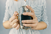 Glass Bottle With Coins In Women's Hands. Blank Black Sticker On Donation Money Jar. Girl In White And Black Striped Shirt Holds Her Savings. Pot For Tips.