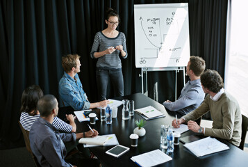Aufkleber - Putting their creative minds to work. Shot of a young woman giving a presentation on a whiteboard to colleagues sitting around a table in a boardroom.