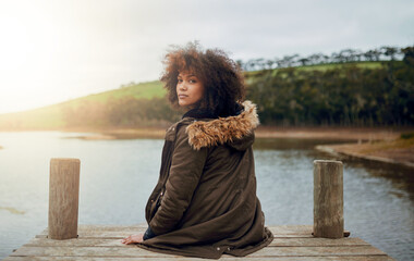 Sticker - Enjoying natures quiet. Portrait of a young woman looking over her shoulder while sitting on a pier.