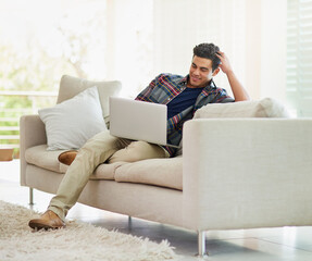 Canvas Print - Comfortable and connected. Shot of a handsome young man using his laptop while relaxing on the sofa at home.