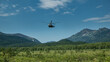 The helicopter comes in to land on an alpine meadow. There is green grass and trees in the valley. A picturesque mountain range against the blue sky. Kamchatka. Nalychevo.