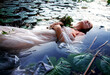 Young sexy woman Lady Ophelia lies with rotten flowers, eyes closed in white dress in the water between water lilies, in the lake