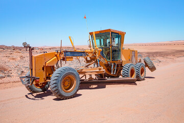 Yellow grader smooths dirt road in namib deserts - Road grader smoothing a dirt road in a rural area - Namibia, Africa