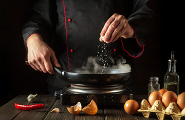 The chef adds salt while cooking eggs in pan. Work environment on kitchen table. Menu idea for a restaurant or hotel.