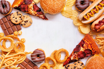 Wall Mural - Junk food frame over a white marble background. Variety of take out and fast foods. Pizza, hamburgers, french fries, chips, hot dogs, sweets. Top down view with copy space.