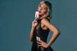 © nazarovsergey - Blonde girl in black leather dress showing two playing cards, posing against blue background. Gambling entertainment, poker, casino. Close-up.