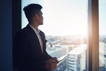 Poster - Look to the future of business. Shot of a young businessman using a digital tablet while looking out the window in an office.