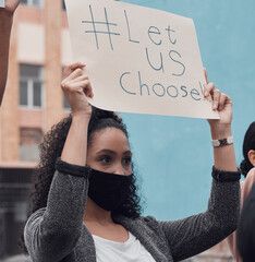 Wall Mural - Let us choose. Cropped shot of an attractive young woman holding up a sign protesting against the covid 19 vaccine with other demonstrators in the background.