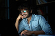 © insta_photos - Happy young indian latin business man or student wearing glasses working, learning online late at night, reading news, watching education webinar at home in dark office using laptop computer at work.