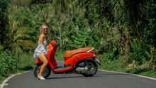 Woman On Red Scooter In White Clothes Drive On Forest Road Trail. Dancing Trip. One Girl Caucasian Tourist In Sunglasses Dance, Relax, Rest Near Motorbike. Asia Thailand Ride Tourism. Motorcycle Rent.