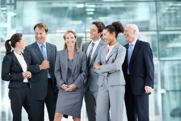 Wall Mural - Supported by her proud team of coworkers. Positive group of businesspeople standing together and smiling while surrounding a coworker - portrait.