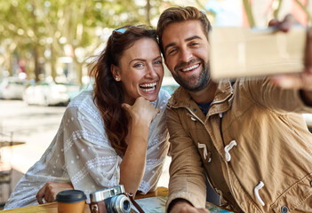 Sticker - Guess where we are. Shot of a happy tourist couple taking a selfie while relaxing at a sidewalk cafe together.