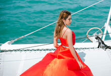 Fashion Model In Beautiful Luxury In Fluttering Red Dress, Asian Woman In Long Flying Evening Dress Looking Away On The Luxury Boat Open Sea In Summer. People Lifestyle,Holiday Outdoors Vacation Trip.