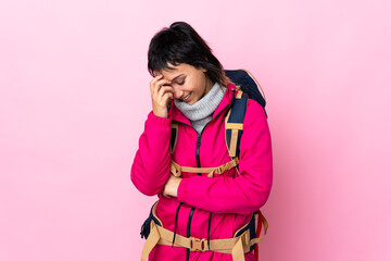 Wall Mural - Young mountaineer girl with a big backpack over isolated pink background laughing