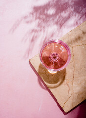 Wall Mural - Pink champagne in glass on luxury marble table with palm shadow. Summer beach cocktail party with  rose wine alcohol beverage on textured background with tropical plant shade. Top view.