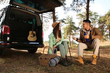 Canvas Print - Couple with thermos and picnic basket resting in camping chairs outdoors