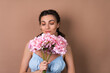 © Анастасия Каргаполов - Portrait of a woman with perfect skin and natural make-up on a beige background with pigtails in a dress holding a bouquet of pink flowers
