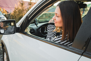 Happy woman driving white car, lady smiling, looking to mirror. Successful girl in automobile. 