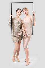 Sticker - Portrait of stylish young sisters with photo frame on light background