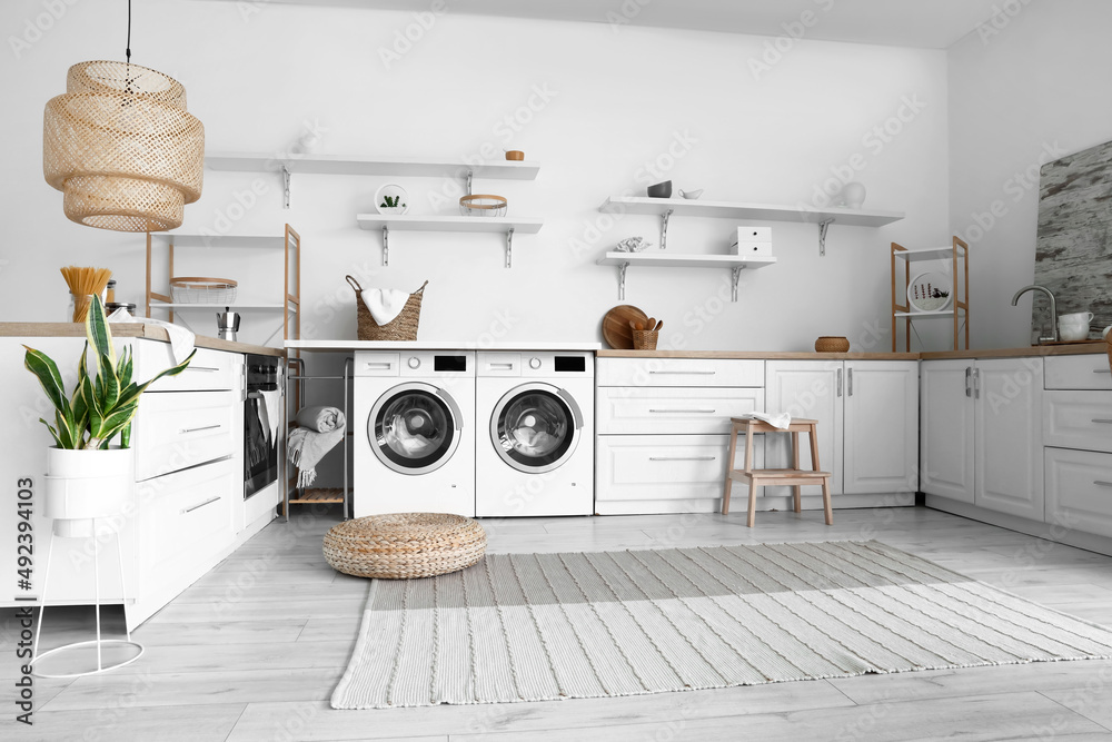 Interior of light kitchen with washing machines, laundry basket and white counters