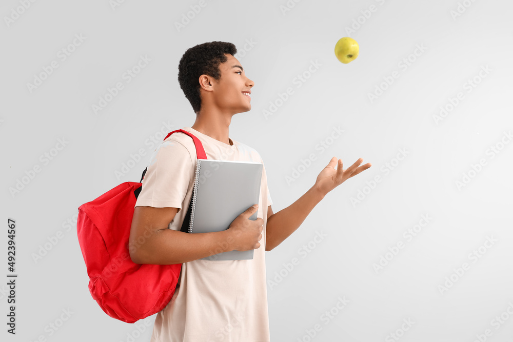 Male African-American student with notebook, backpack and apple on light background