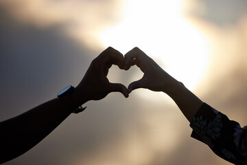 Wall Mural - The best thing to hold onto in life is each other. Shot of an unidentifiable couple making a heart shape with their hands at sunset.