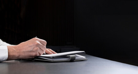 Poster - Businessman hands writing in business planner ove black background with copy space for text.